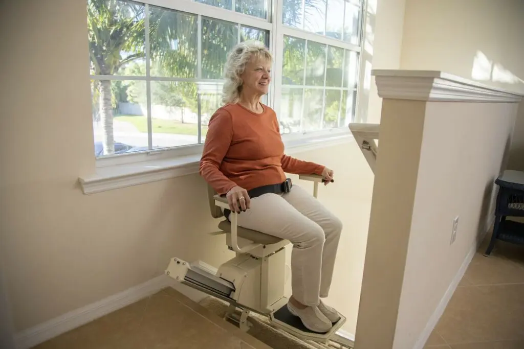 Elderly woman comfortably sitting on a stair lift to go down stairs in her Waterford, MI home.