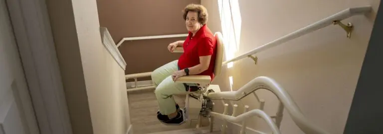 Elderly woman riding a stair lift down a flight of stairs in her home.
